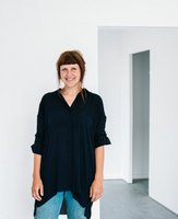Anne-Lena in schwarzer Bluse und Jeans in einem weißen Raum, im Hintergrund mehrere Durchgänge ohne Tür hintereinander