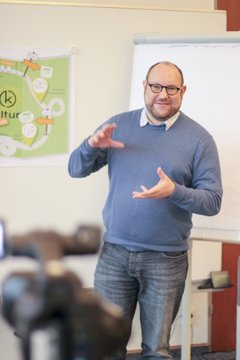 Tobias im blauen Pulli vor einem Flipchart