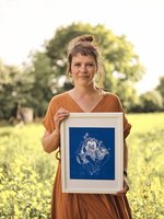 Katja im roten Kleid vor einem gelben Rapsfeld mit einer blauen Zeichnung in der Hand