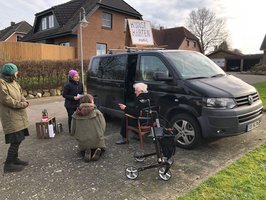 4 Menschen unterschiedlichen Alters vor dem VW-Bus auf einer Parkfläche im Gespräch