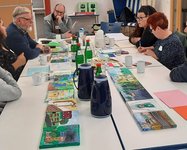 Menschen sitzen an einem Tisch mit selbstgemalten Bildern