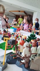 Der Workshopleiter erklärt die neue Aufgabe, im Vordergrund eine Playmobillandschaft die ein Musical darstellt