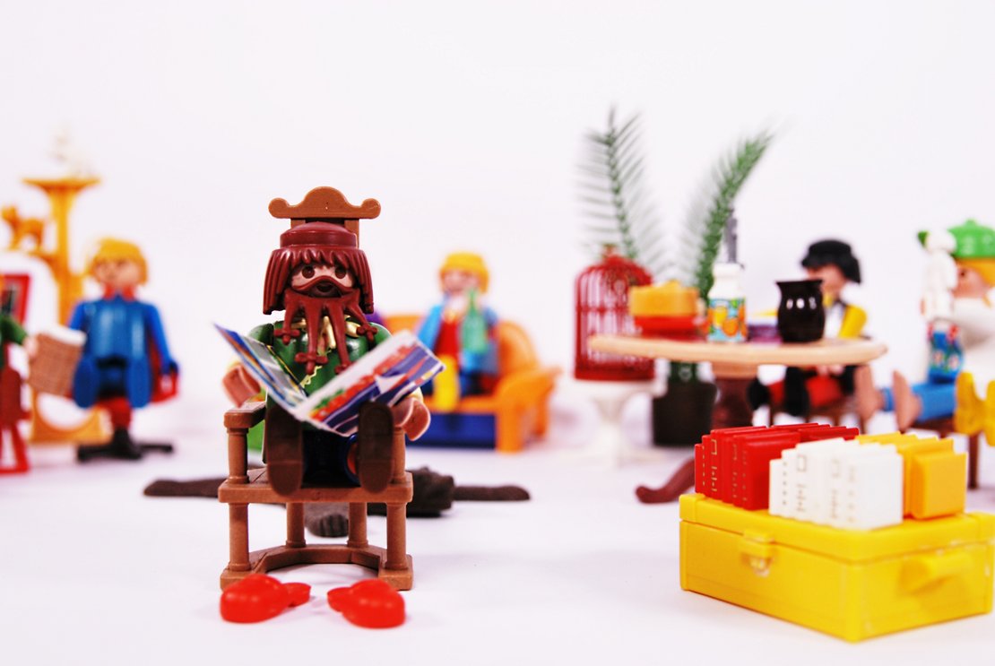 Kulturpaket Im Wohnzimmer Das Publikum sitzt verteilt auf Sofas und Sesseln, auf einem Tisch stehen Snacks, ein/e Autor'in liest aus ihrem/seinem Buch vor.